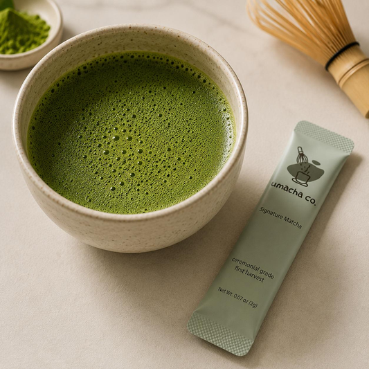 Whisked green matcha in a ceramic bowl beside a bamboo whisk and single-serve matcha stick