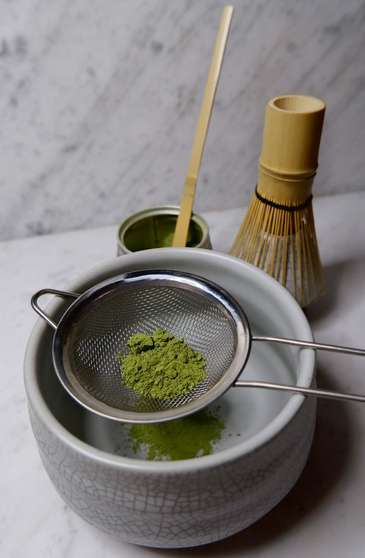 Sifting matcha powder over a ceramic bowl to help make matcha smooth