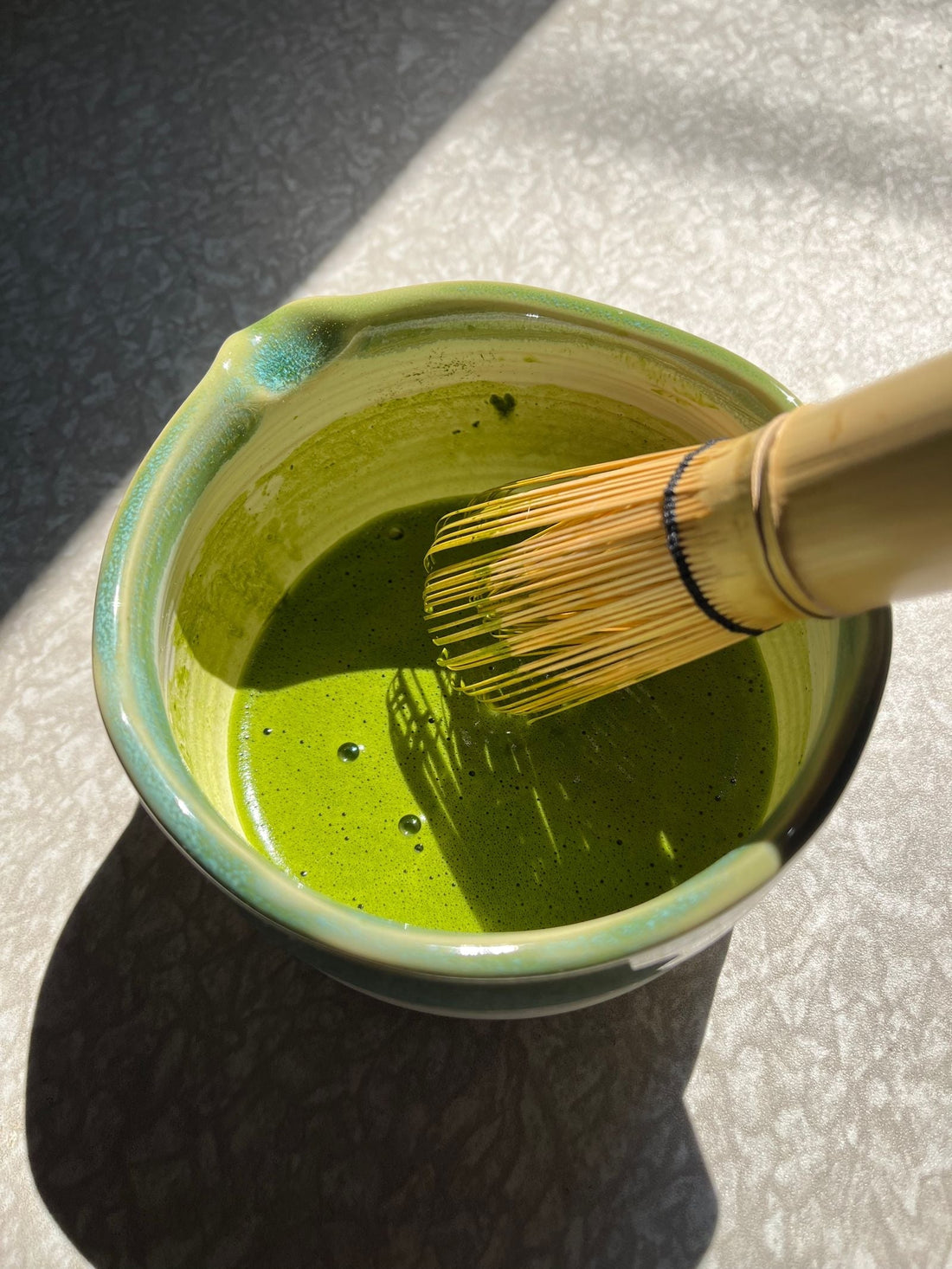Ceremonial grade matcha in a ceramic bowl with a bamboo whisk under natural sunlight