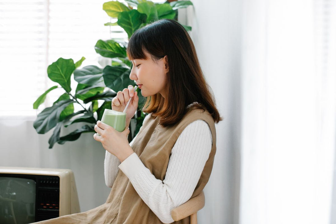 Woman enjoying a pale green matcha latte beside houseplants in natural morning light
