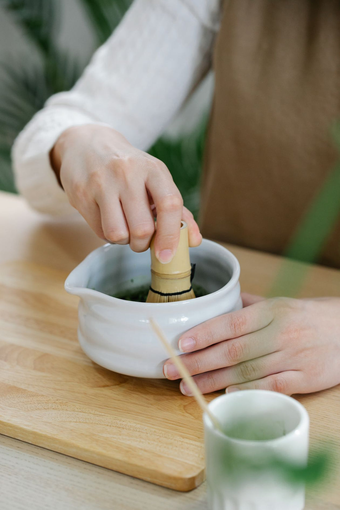 Hands whisking green matcha in a white ceramic bowl on a wooden table