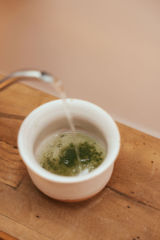 Matcha water temperature step with hot water pouring into green powder in a ceramic bowl