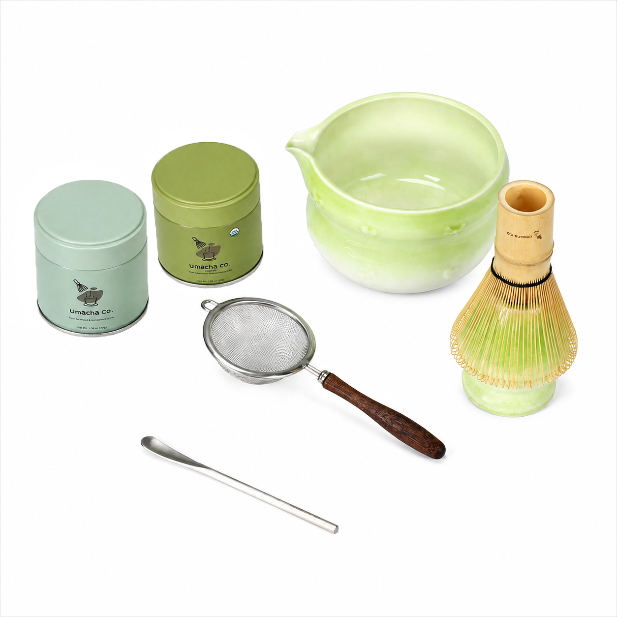 A green tea preparation set on a white background, including two metal tea tins, a pale green ceramic bowl, a bamboo whisk, a metal strainer with a wooden handle, and a metal spoon.